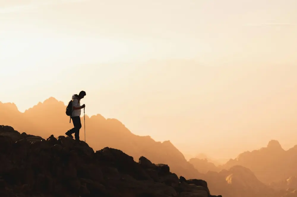 A person in silhouette hiking on a rocky ridge during golden hour, illustrating inspiration and discovery